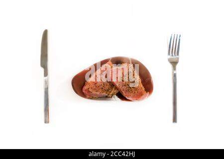 Raw tuna steaks marinated in gourmet sauce with black pepper, lemon and olive oil on silver plate with fork and knife isolated on white background. Cl Stock Photo