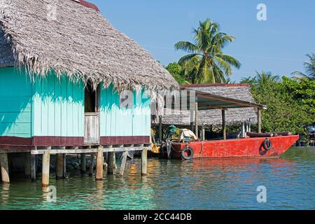 Red boat and wooden house on stilts with thatched roof on the Dulce River / Rio Dulce, Izabal Department, Guatemala, Central America Stock Photo