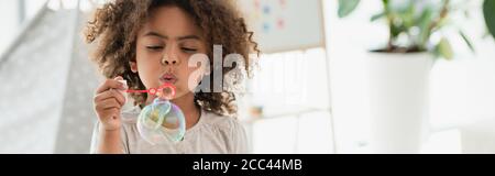 panoramic shot of curly african american kid blowing soap bubbles Stock Photo