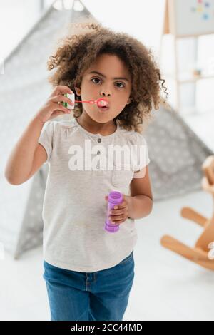 curly african american kid blowing soap bubbles and looking at camera Stock Photo