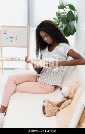 african american woman reading book while sitting on sofa Stock Photo