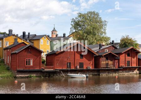 Old red-ocher storage buildings on the riverbank of Porvoonjoki and Old Town wooden houses in the background in Porvoo, Finland Stock Photo
