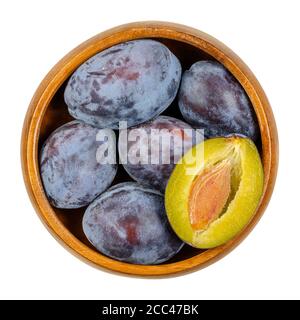 Ripe European plums with cross section of one fruit in a wooden bowl. Freestone fruit with purple, violet and black skin, also called Damson. Stock Photo