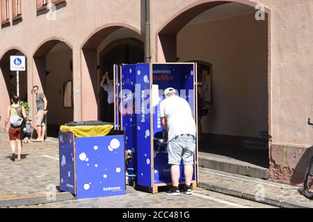 Man cleaning his hand with disinfecting solution in blue stand during corona pandemic before entering local market near Freiburg Minster. Stock Photo