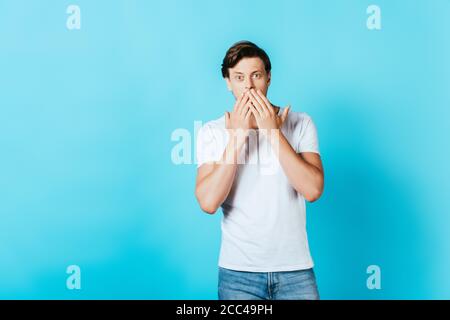Shocked young man in white t-shirt looking at camera on blue background Stock Photo