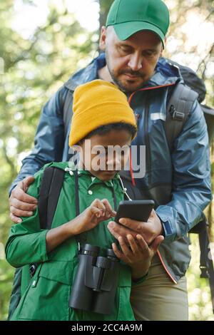 Father showing to his son how to use mobile phone during their hiking in the forest Stock Photo