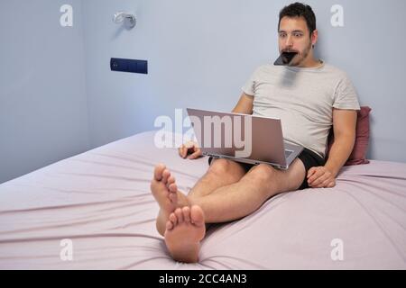 Young adult with his smartphone in his mouth desperate. Working from home concept. Stock Photo