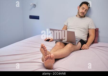 Young adult asleep while he is working on his laptop on bed. Working from home concept. Stock Photo