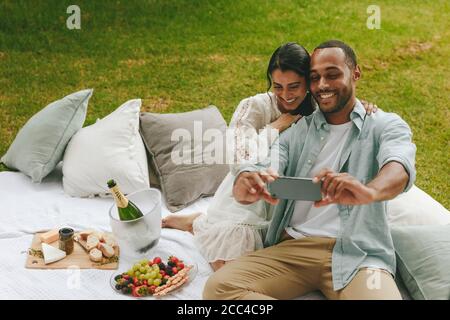 Loving young couple taking selfie at park. Beautiful couple on picnic taking self portrait at park. Stock Photo