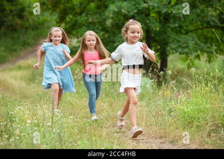 Memories. Kids, children running on green forest. Cheerful and happy boys and girs playing, laughting, running through green blooming meadow. Childhood and summertime, sincere emotions concept. Stock Photo