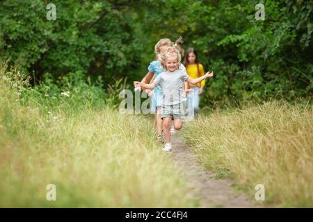 Carefree. Kids, children running on green forest. Cheerful and happy boys and girs playing, laughting, running through green blooming meadow. Childhood and summertime, sincere emotions concept. Stock Photo