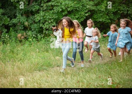 Carefree. Kids, children running on green forest. Cheerful and happy boys and girs playing, laughting, running through green blooming meadow. Childhood and summertime, sincere emotions concept. Stock Photo