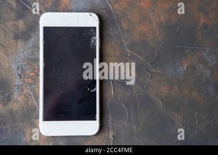 White phone with a broken screen on dark background Stock Photo