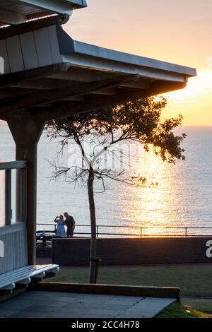 Couple taking a selfie in front of the sun setting over the sea on the east coast at Hunstanton. Stock Photo