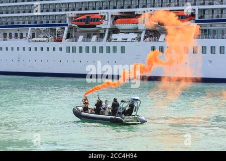 A man in an inflatable boat sets off a smoke flare in a simulated emergency. In the background is a cruise liner. Auckland, New Zealand, 1/25/2019 Stock Photo