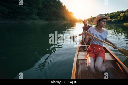 Young woman paddling canoe, couple enjoy boat ride on the summer sunset Stock Photo