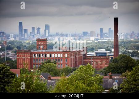 Grade II listed large red brick textile  Devon Mill in Oldham with the Manchester Skyline behind Stock Photo