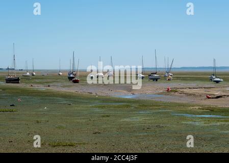 People and yachts out on the mud flats in Leigh on Sea, Essex, UK. At low tide the sea retreats a long way out and people walk out. Masts Stock Photo