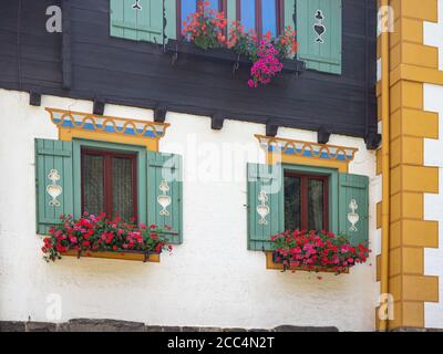 Facade of traditional austrian house with ancient wooden windows and blinds or shutters. Colorful geraniums hang from the window. Stock Photo