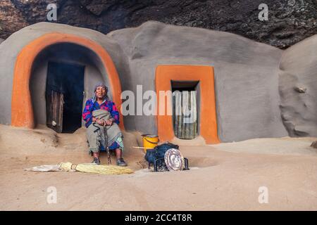 BEREA, LESOTHO - AUGUST 23, 2012: Indigenous woman in front of cave dwellings made out of mud in the district of Berea, Lesotho Stock Photo