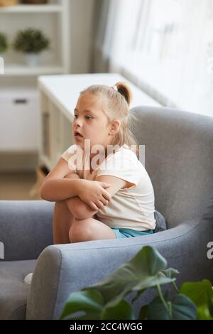 Little girl with down syndrome sitting on armchair and resting in the living room Stock Photo