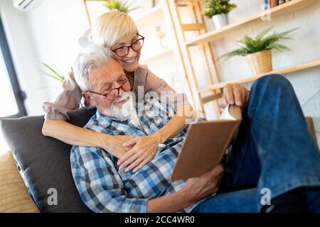 Beautiful old couple is reading a book and smiling at home Stock Photo