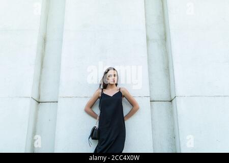 Outdoors portrait of trendy pretty girl posing on the white wall in the city. Stock Photo