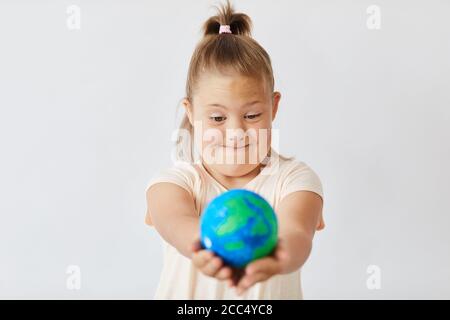 Girl with down syndrome looking at the Earth planet in her hands isolated on white background Stock Photo