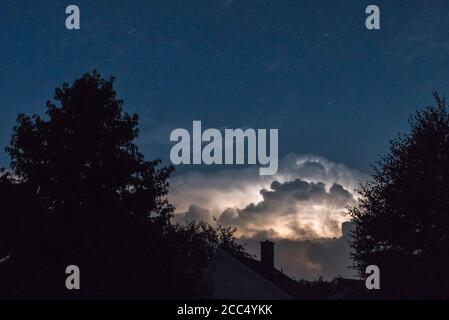 A thundercloud lit by lightning flashes beneath a clear starry night sky, Wales, UK Stock Photo