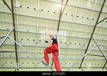 Young electrician connecting electrical cables inside the lit by sun solar modules. Ecology power conservation concept. Green ecological power energy generation. Stock Photo