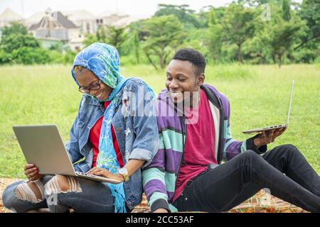 Young African students sitting in a park working on a college task together on their laptops Stock Photo