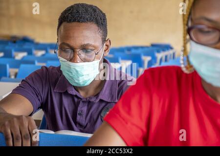 Shallow focus of two young African students wearing facemasks and studying in a classroom Stock Photo