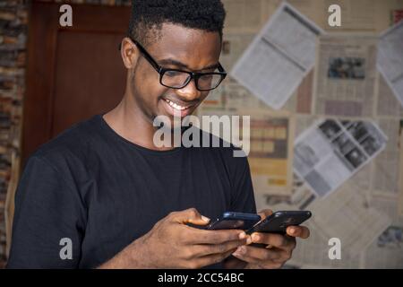 Shallow focus of a young African male with glasses using two phones in a room Stock Photo