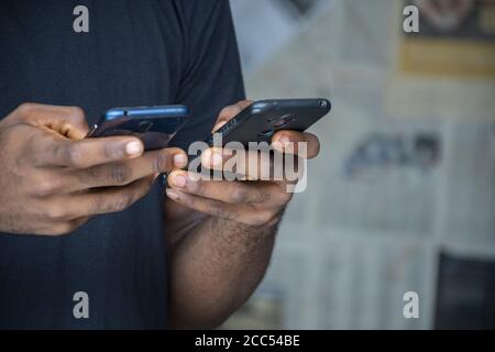 Closeup of a young African male using two phones in a room Stock Photo