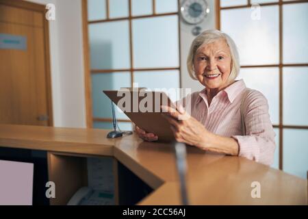 Happy stylish lady in pink shirt standing at the reception of dental clinic Stock Photo