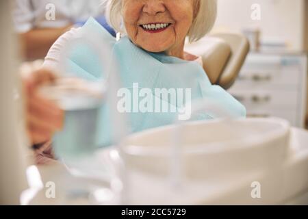 Smiling female sitting on the dentist chair while having care to the teeth Stock Photo