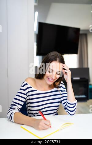 Thoughtful woman writing in her kitchen Stock Photo