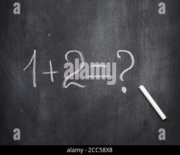 math example written in white chalk on a black chalk board and white chalk, one plus two Stock Photo