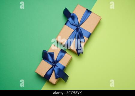 two rectangular boxes wrapped in brown paper and tied with a silk ribbon with a bow, gift on a green background, top view Stock Photo