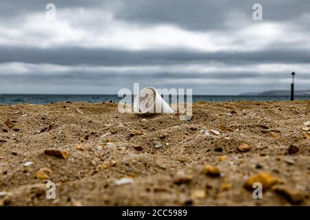 Plastic Pollution: Styrofoam Cup left by tourists on the beach. Cruise ship in background. Bournemouth, UK. Stock Photo