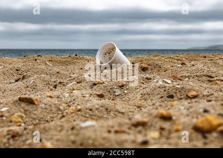 Plastic Pollution: Styrofoam Cup left by tourists on the beach. Cruise ship in background. Bournemouth, UK. Stock Photo