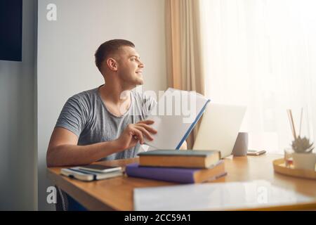 Handsome young guy sitting with documents at home and dreaming Stock Photo