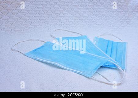 Three disposable surgical face masks lying on white textile background Stock Photo