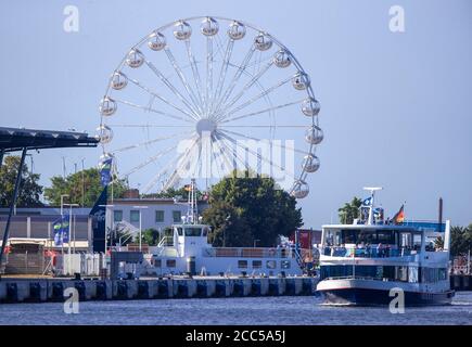 Rostock, Germany. 12th Aug, 2020. An excursion ship sails on the sea channel at the cruise ship terminal in the Baltic resort of Warnemünde. A Ferris wheel is built on the middle mole. Credit: Jens Büttner/dpa-Zentralbild/ZB/dpa/Alamy Live News Stock Photo