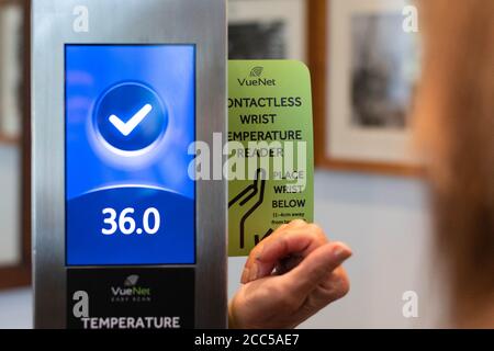covid 19 temperature screening - woman taking her temperature using a contactless wrist temperature reader  during coronavirus pandemic - UK Stock Photo