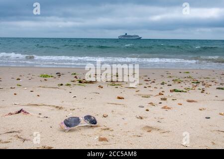 Plastic Pollution: Dropped sunglasses with cruise ship in the background. Bournemouth, UK. Stock Photo