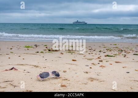 Plastic Pollution: Dropped sunglasses with cruise ship in the background. Bournemouth, UK. Stock Photo