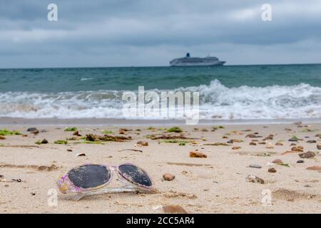 Plastic Pollution: Dropped sunglasses with cruise ship in the background. Bournemouth, UK. Stock Photo