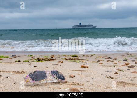 Plastic Pollution: Dropped sunglasses with cruise ship in the background. Bournemouth, UK. Stock Photo