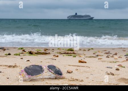 Plastic Pollution: Dropped sunglasses with cruise ship in the background. Bournemouth, UK. Stock Photo